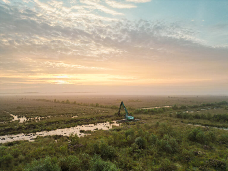 Natuurherstel en Waterbouw - Natuurherstel werkzaamheden Fochteloërveen met uitzicht op veel van landschap. Midden WK220 NG-5 werkzaam bij zonsopkomst in veengebied