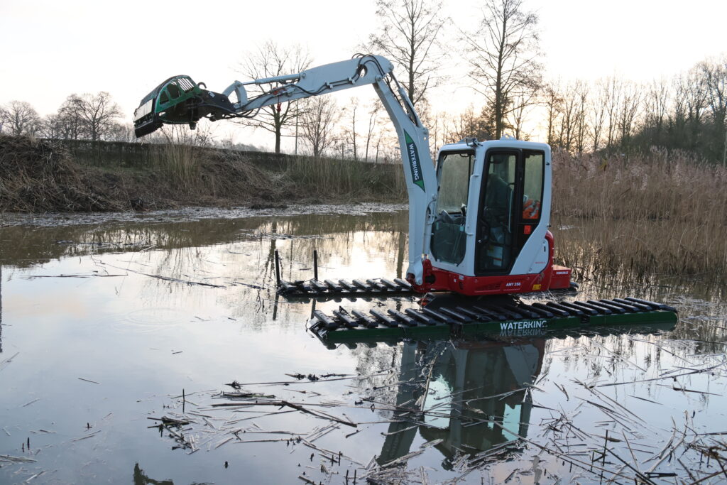 Natuurherstel en Waterbouw, Rental Referentie, Zicht: Silhouet WK20 NG-A werkzaam in vijver om riet te maaien, maaikorf aan giek