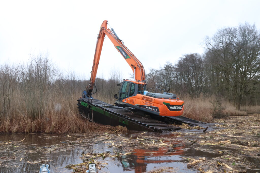 Natuurherstel en Waterbouw, Rental Referentie, Zicht: Achterzijde WK220 NG-5 uit water rijdend met frees aan giek voor natuurherstelproject