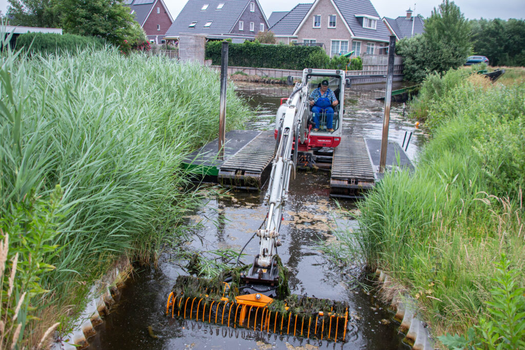 Natuurherstel en Waterbouw, Rental Referentie, Zicht: beunbak op kant, WK55 NG-A zijpontons aanwezig met sputpalen, exoten verwijderen uit kanaal woonwijk, maaikorf aan giek en mogelijk om smalle doorgangen vrij te maken van exoten
